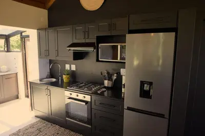 a kitchen with white cabinets and a stainless steel refrigerator at Cozy House & Studio with Sea and Mountain Views in Bettyʼs Bay