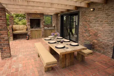 a patio with a wooden table and benches and a brick wall at Cozy House & Studio with Sea and Mountain Views in Bettyʼs Bay