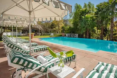 a row of lawn chairs with umbrellas next to a swimming pool at Franschhoek Manor in Franschhoek