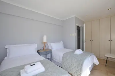 a white bedroom with two beds and a table at Church View Lux Apartment in Stellenbosch