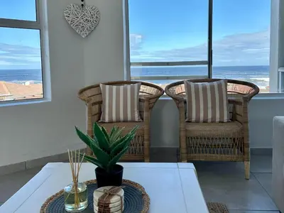 two wicker chairs and a table in a room with windows at Seaside Serenity in Hermanus