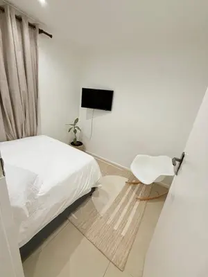 a white bedroom with a bed and a chair at Three Bedroom Apartment in Cape Town