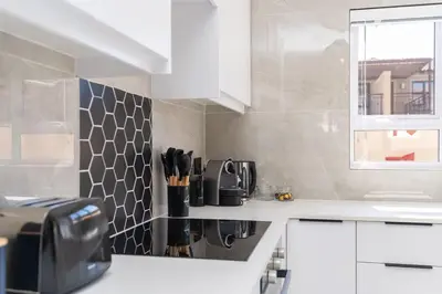 a kitchen with white cabinets and a black and white tile wall at Surfside Haven, 3 Bed Townhouse in Cape Town