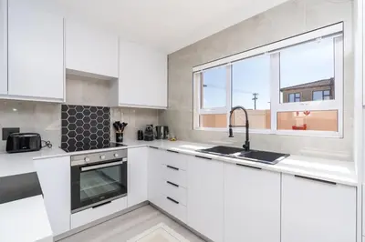 a white kitchen with a sink and a window at Surfside Haven, 3 Bed Townhouse in Cape Town