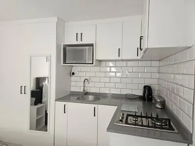 a kitchen with white cabinets and a sink and a refrigerator at Cozy Private Studio in Cape Town