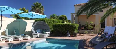 a pool with chairs and umbrellas next to a house at Somerset Wineland Apartments & Wellness in Somerset West