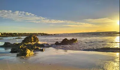 a beach with rocks in the water at sunset at C es Cape in Pringle Bay