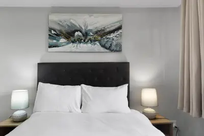 a bedroom with a white bed with a painting above it at Two Bedroom Luxury Apartment, Century City - BackUp Power in Cape Town