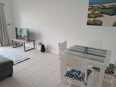 a living room with a table and a desk with a laptop at 8 Marina Sands beach apartment in Cape Town