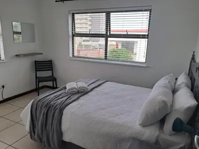 a bedroom with a bed with a window and a chair at 8 Marina Sands beach apartment in Cape Town