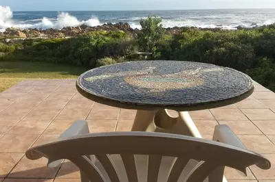 a table and a chair with the ocean in the background at Heaven's Door in Bettyʼs Bay
