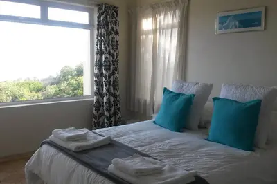 a bedroom with a bed with blue pillows and a window at Heaven's Door in Bettyʼs Bay