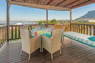 a table and chairs on a deck with the ocean at Whispering Waves in Hermanus