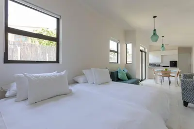 a white bedroom with a large bed and a living room at Lux Private Garden Studio - Sunset Beach in Cape Town