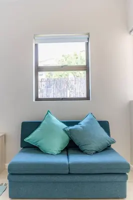 a blue couch with two pillows sitting under a window at Lux Private Garden Studio - Sunset Beach in Cape Town