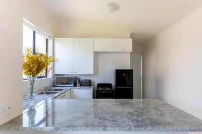 a kitchen with white cabinets and a black refrigerator at Lux Private Garden Studio - Sunset Beach in Cape Town