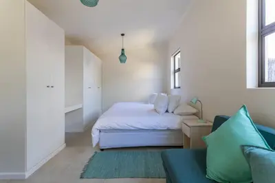 a small bedroom with a bed and a couch at Lux Private Garden Studio - Sunset Beach in Cape Town
