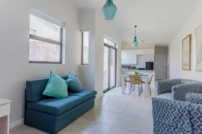 a living room with a blue couch and a kitchen at Lux Private Garden Studio - Sunset Beach in Cape Town