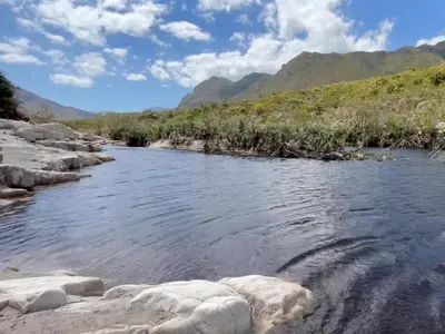a river with rocks and mountains in the background at The River Retreat Kogelberg in Kleinmond