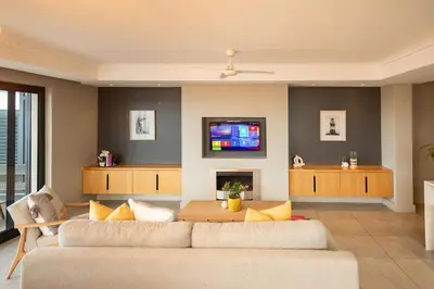 a living room with two couches and a tv at Ocean Family Deluxe, Hermanus Waterfront Apartments in Hermanus