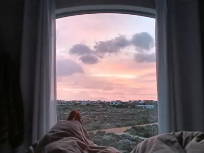 a person laying in bed looking out of a window at KLIPWERF Bettys Bay in Bettyʼs Bay
