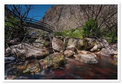 a creek with a bridge and rocks and a mountain at KLIPWERF Bettys Bay in Bettyʼs Bay