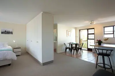 a bedroom with a bed and a dining room with a table at Luxury Studio sleeps up to 3 adults - Sunset Beach in Cape Town