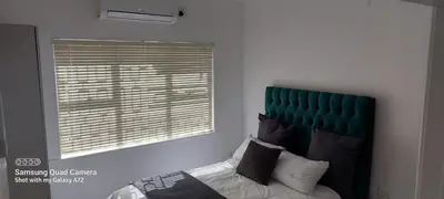 a bedroom with a bed with a green headboard and a window at COMFORT LODGE milnerton, Cape Town in Cape Town