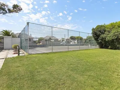 a chain link fence with a tennis court at Elana Beachfront Condo in Strand