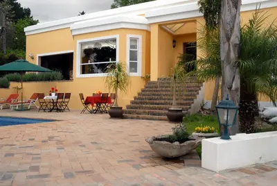 a yellow house with a patio with tables and chairs at Big6 Guesthouse in Somerset West