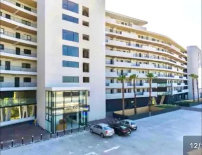 a large building with cars parked in a parking lot at Stylish waters edge apartment in Cape Town