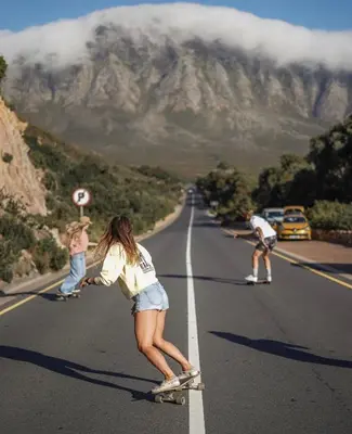 a group of people skateboarding down a road with a mountain at Awesome room in surf house in Hermanus