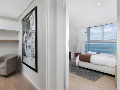 a bedroom with a bed and a chair and a window at Sunsets on Beach Strand in Cape Town