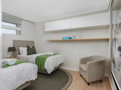 a bedroom with two beds and a chair in it at Sunsets on Beach Strand in Cape Town