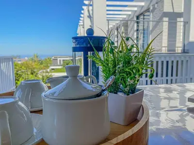 a table with white dishes and a plant on a balcony at Chanteclair Re-Energised 1 Bed 1 Bath in Hermanus