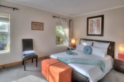 a bedroom with a bed and a chair and two windows at TUSCAN VILLA FELICE near West Coast in Cape Town