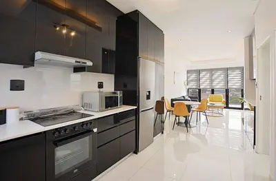 a kitchen with black cabinets and a table with chairs at Greystone Executive Apartments in Cape Town