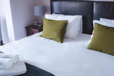 a bed with white sheets and green pillows at Ilanga Du Cap Hotel in Cape Town