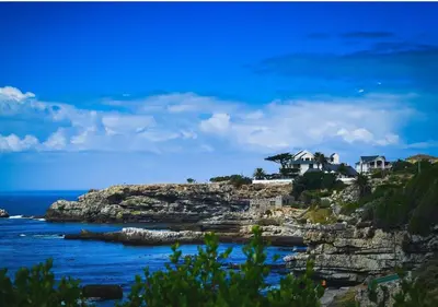 a house on top of a rocky hill next to the ocean at A Short Walk to the Cliffs in Hermanus