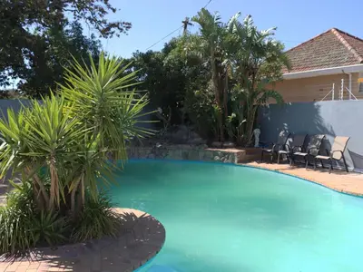 a swimming pool with palm trees in a yard at West Gemini Guesthouse in Cape Town