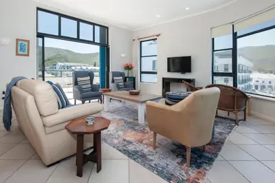 a living room with a couch and chairs and a tv at Seafront Penthouse - Marine Court Hermanus in Hermanus
