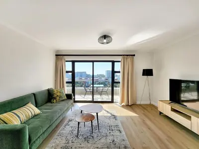 a living room with a green couch and a television at Canal, Mountains, Sea Views, Pool, Gym, Parking, Wifi in Cape Town