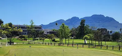 a golf course with a building and mountains in the background at Stellenbosch Paradijs Cottage Paradyskloof in Stellenbosch