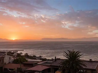 a sunset over the ocean with houses and a city at Phezulu Manor, Panoramic Views, Serviced Retreat in Gordonʼs Bay