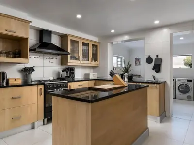 a large kitchen with wooden cabinets and a black counter top at Phezulu Manor, Panoramic Views, Serviced Retreat in Gordonʼs Bay