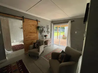a living room with two chairs and a sliding glass door at Mosselberg Garden Gottage in Hermanus