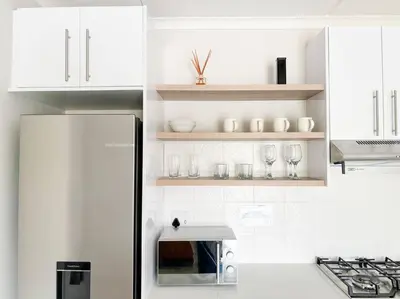 a white kitchen with a refrigerator and glasses on shelves at Coastal Beach & Mountain Retreat in Cape Town