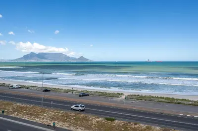 a road with cars on it next to a beach at 2 Bedroom Apartment - Blouberg Beachfront in Cape Town