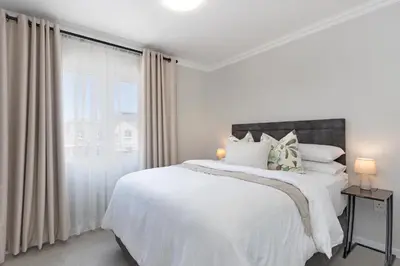 a white bedroom with a large bed and a window at Elegant apartment near beach in Cape Town