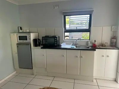 a kitchen with white cabinets and a sink and a microwave at Casa on Alamein in Cape Town